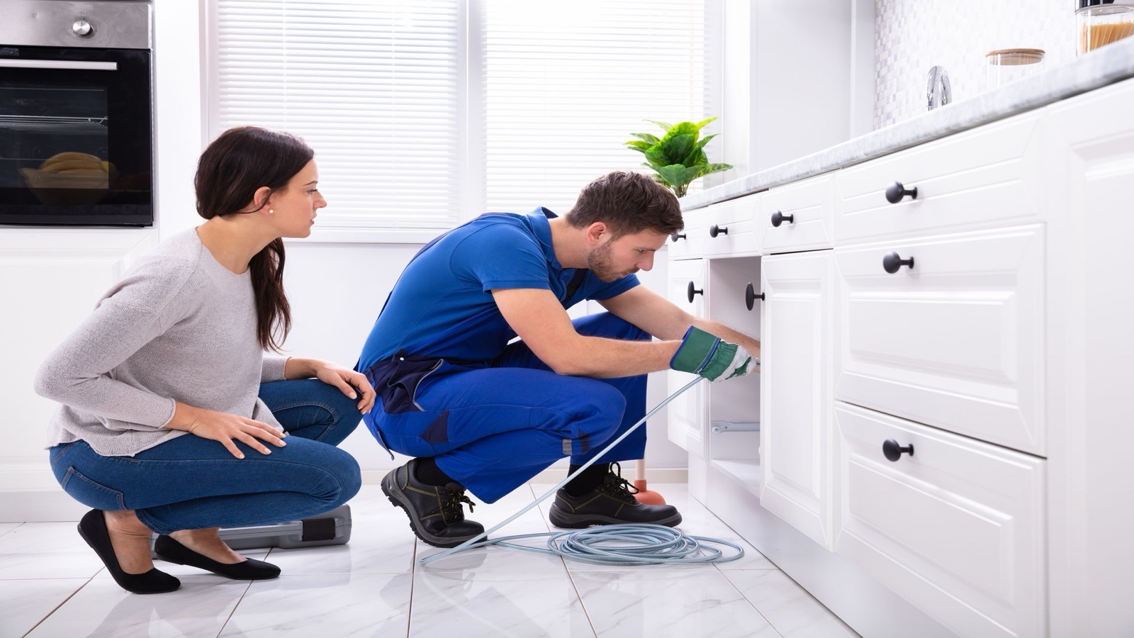 Plumber clearing a kitchen drain while a homeowner observes